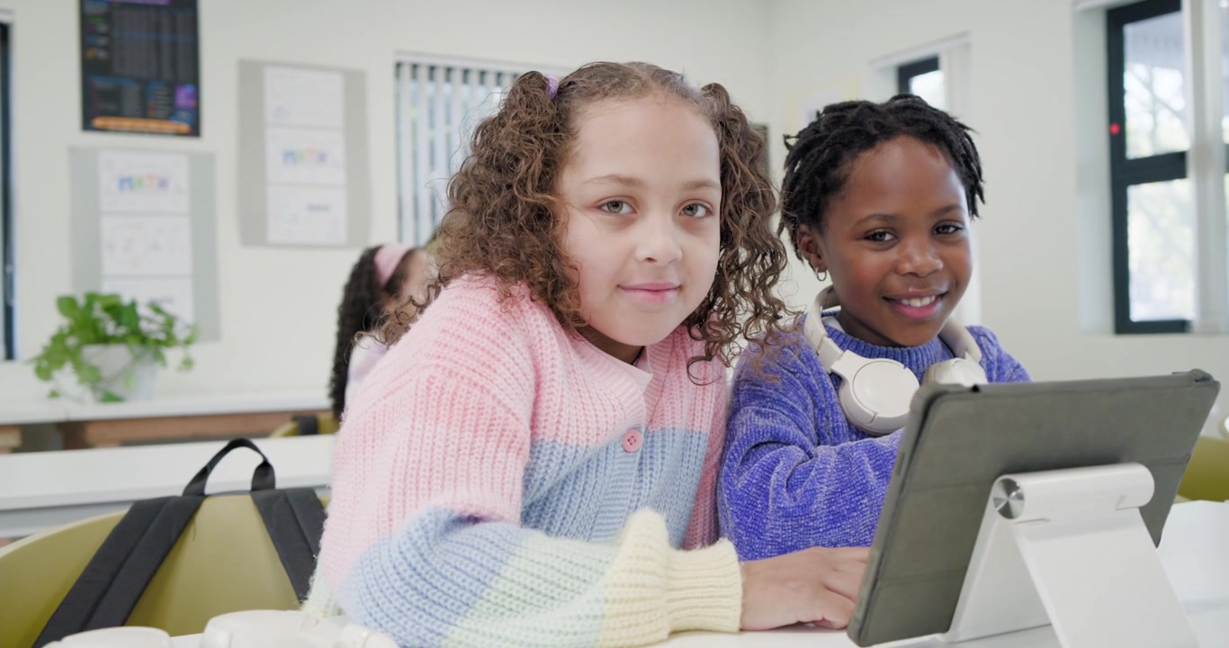 Diverse youth females reacting to tablet lesson in class, left tapping tablet while right watching