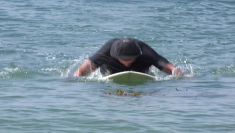 a middle aged surfer dude paddles his board in the waves and then leaves the water