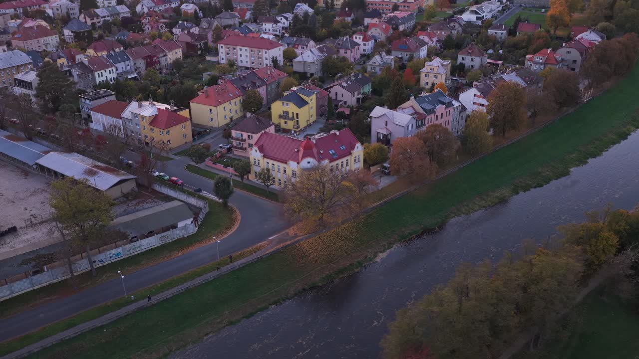 A car driving down a street past houses and a river in the city. Evening view from a drone