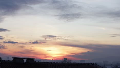 time-lapse of a colorful sunrise, hidden behind clouds, with a red tile roof in the foreground