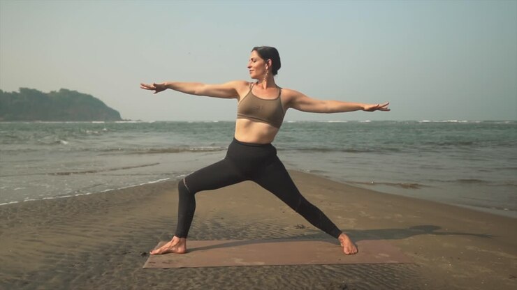 Donne che eseguono la posizione yoga del Guerriero Due sulla spiaggia