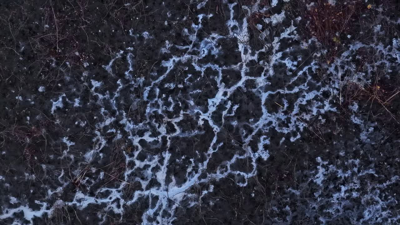 Dark, muddy earth covered with abstract, vein-like frost patterns
