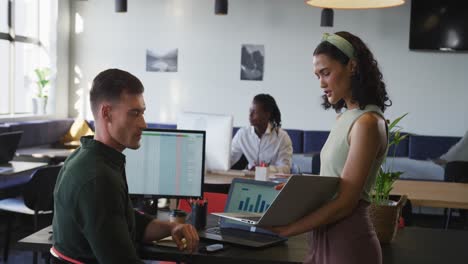 Diverse-business-people-discussing-work-and-using-laptop-at-office