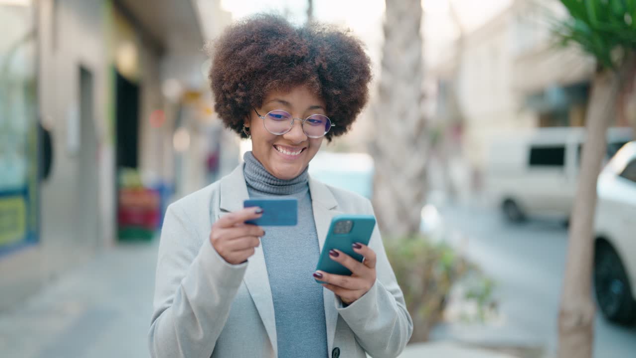 mujer afroamericana usando teléfono inteligente y tarjeta de crédito en la calle