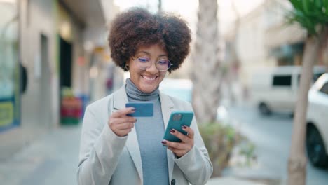 african american woman using smartphone and credit card at street