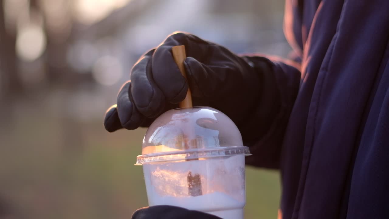 Man's hands mixing the coffee with a bamboo straw in sunlight