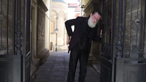 elderly man with back pain leaning on gate in old alley with historical architecture