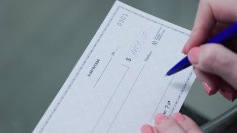 business woman hand signs and filling bank check for one thousand 1000 dollars