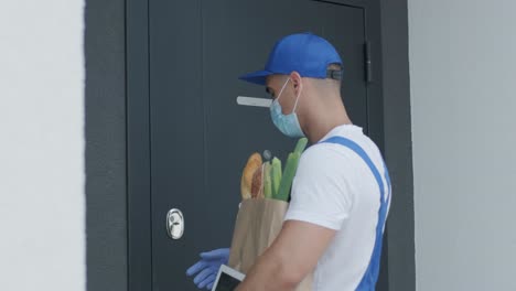 young courier wearing protective mask and gloves deliver a shopping package with food directly to a customer home with safety. food delivery, home delivery in quarantine