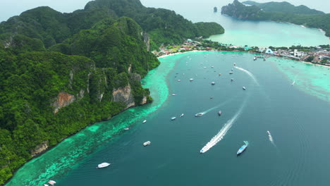 Boats-anchored-and-speed-past-with-wake-along-sheer-tropical-cliffs-of-koh-phi-phi-thailand