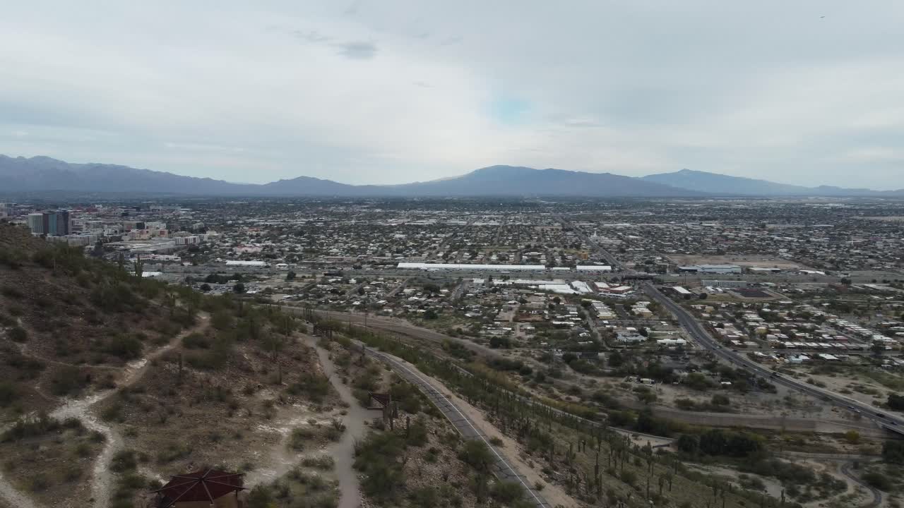 Ampio panorama aereo con drone della valle di Tucson, Arizona, con fitti quartieri desertici e catene montuose che si estendono all'orizzonte sotto cieli nuvolosi.