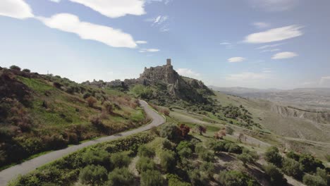 Drone-flying-forwards-and-upwards-over-a-road-towards-the-old-ruins-of-Craco-on-a-hill-in-the-south-of-Italy-in-4k