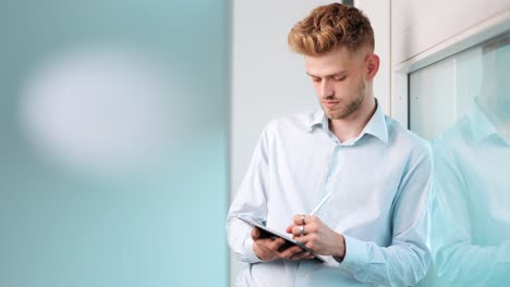 Modern-Workspace:-Young-Businessman-with-iPad-Writing-Notes