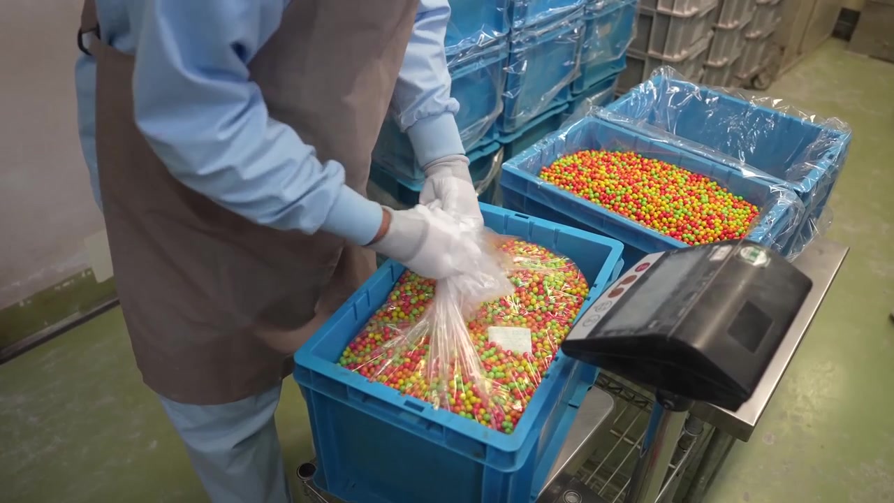 Gloved worker bagging finished colorful coated pellets from a blue crate