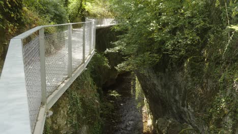 a white bridge crosses an alpine mountain with a river along green forested area