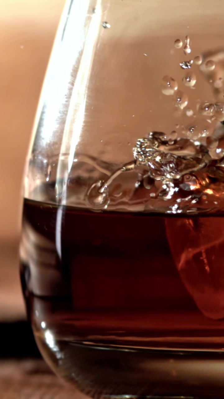 Primo piano di un cubetto di ghiaccio che schizza in un bicchiere di whisky al rallentatore