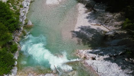 turquoise-blue-waterfall-flowing-into-crystal-clear-river-in-Dolomites-forest-of-Italy-on-summer-day,-aerial-top-down