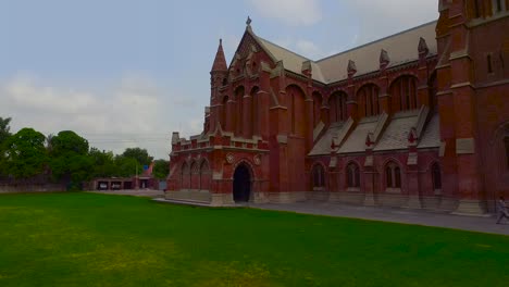 una vista aérea en ángulo bajo de una hermosa y antigua iglesia hecha con ladrillos rojos, pasto verde y autos estacionados en el estacionamiento de la iglesia
