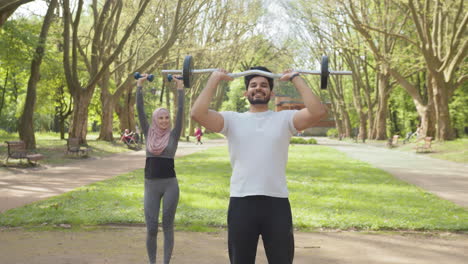 couple working out in a park with barbell and dumbbells