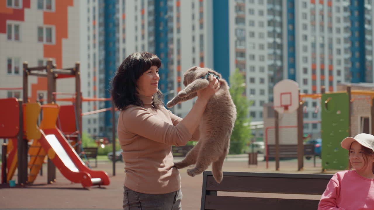 Caucasian Woman Raises Rabbit High Near Playground Slides, Joyful Expression And Bright Sunlight, Playful Celebration That Draws ChildS Attention, Affectionate Adult And Lively Urban Backdrop