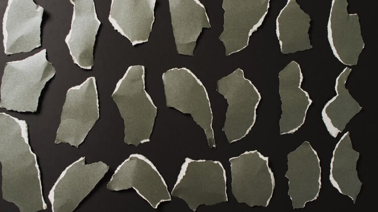 Video of close up of multiple torn piece of green paper on black background