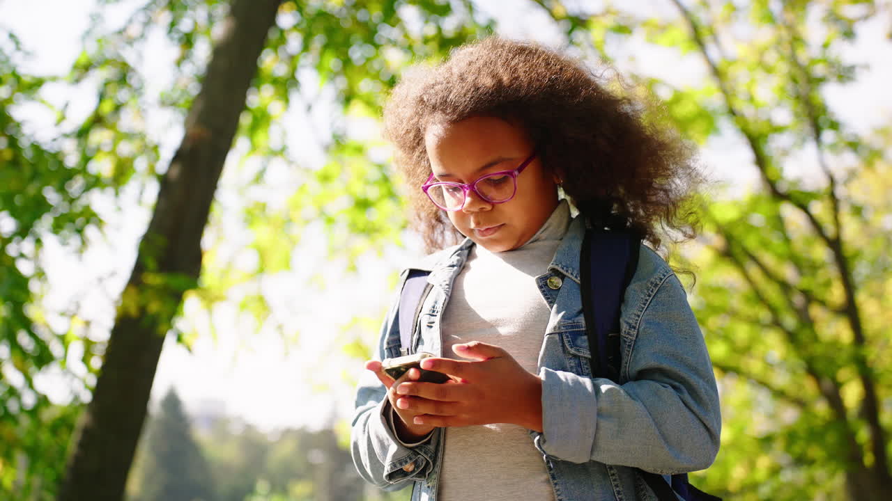 Young Girl with Curly Hair Using Smartphone in a Sunny Park