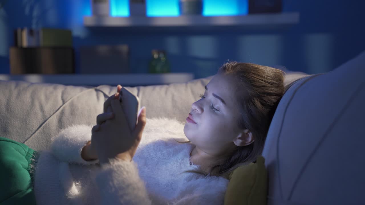 우울한 젊은 여성이 집에서 전화로 문자 메시지를 보내고 있습니다.