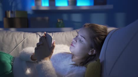 una joven deprimida enviando mensajes de texto por teléfono en casa.