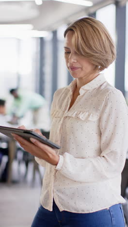 vertical video: holding tablet, woman standing confidently in modern school office environment