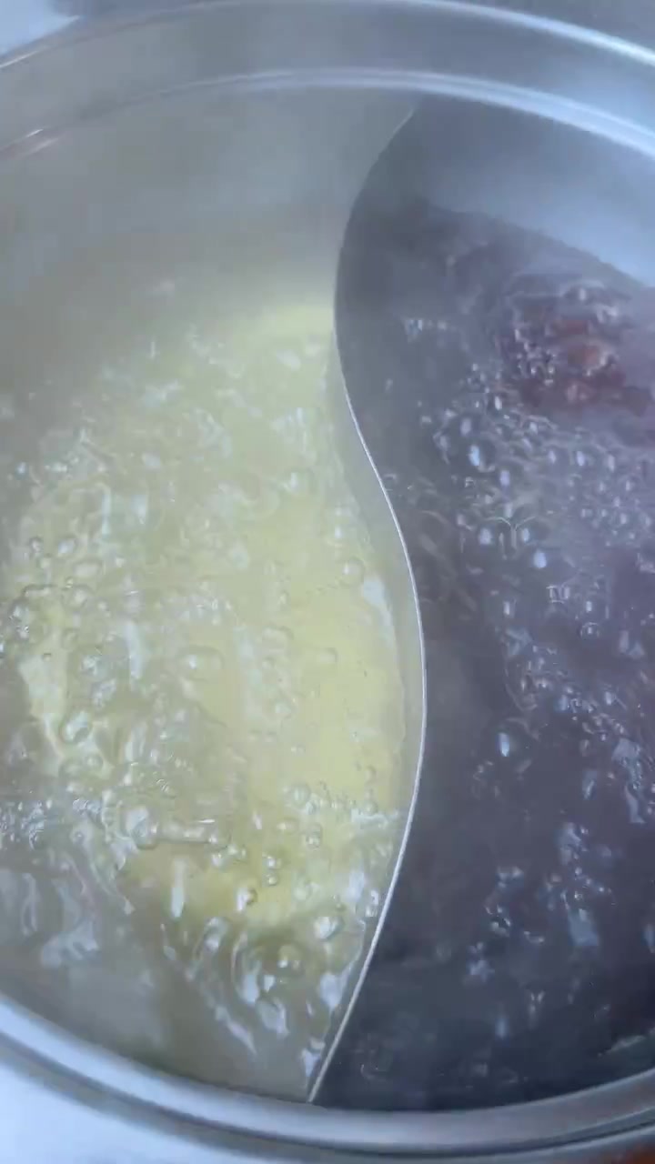 Primer plano de caldos humeantes de olla caliente doble hirviendo vigorosamente, vista cenital, iluminación natural, movimiento mínimo.