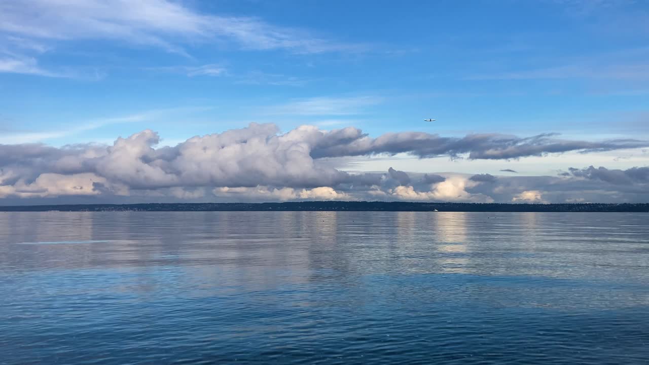 Jet plane flying above the clouds as seen from across the water on a sunny day