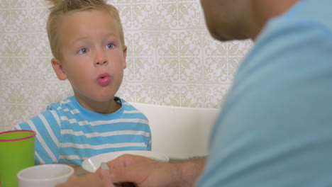 Little-boy-eating-with-his-dad-they-talk-about-something