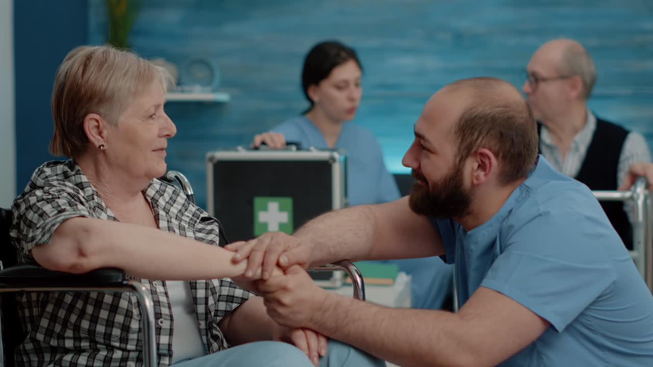 Man nurse holding hands and comforting handicapped pensioner