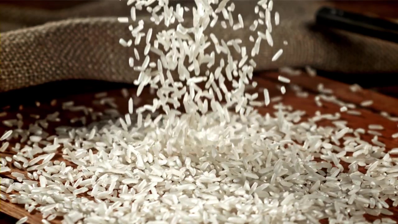 Slowmotion af hvide risgryn, der falder ned på en træoverflade