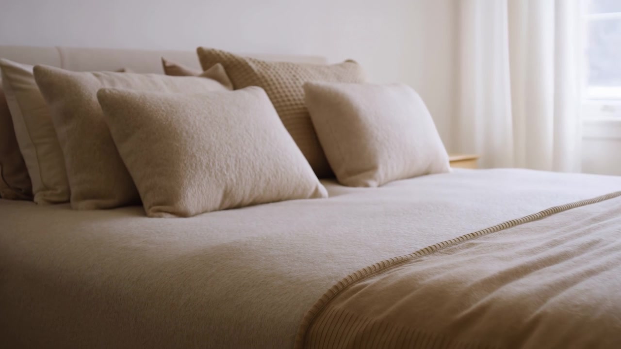 Camera da letto accogliente con cuscini in lino beige. Luce solare soffusa attraverso tende trasparenti, coperta a maglia a strati, testurizzato