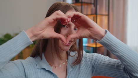 young pretty woman makes symbol of love, showing heart sign to camera, express romantic feelings