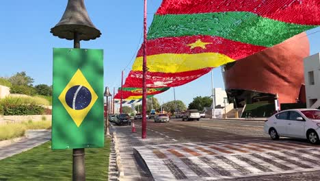 Autos-De-Lujo-Moviéndose-En-La-Ciudad-Vieja-De-Katara-En-Doha-Qatar-Y-Arte-De-Diseño-De-Banderas-Ondeando-Por-El-Viento-Cerca-De-La-Playa-Y-Resorts-En-Un-Día-Tranquilo-Y-Pacífico-En-La-Tarde-Cerca-Del-Atardecer-Para-Recibir-Invitados-De-La-Copa-Del-Mundo