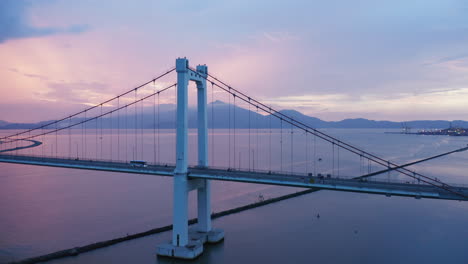 an aerial drone flight over a suspension bridge with mountains int he background