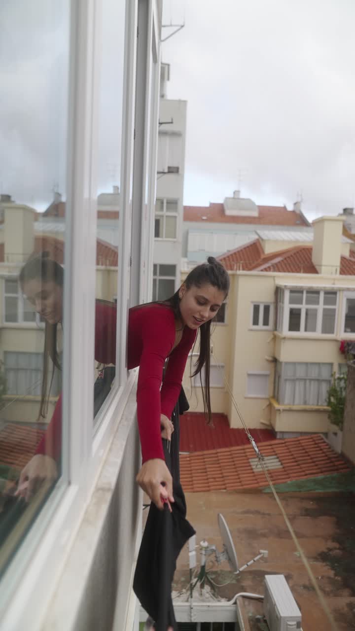 Woman Hanging Clothes from Balcony Window