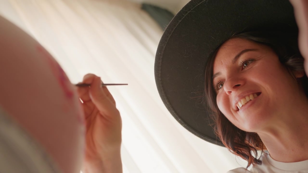 Donna sorridente con cappello intenta a dipingere in modo creativo