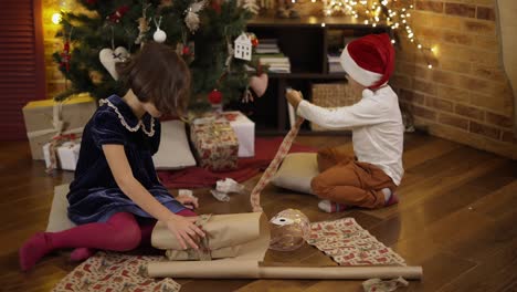 Linda-Niña-Y-Su-Hermano-Envolviendo-Regalo-De-Navidad