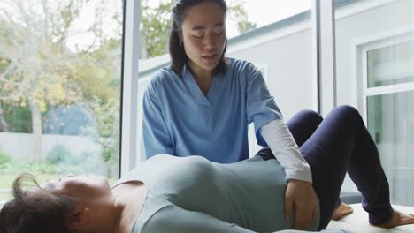 Asian-female-physiotherapist-treating-female-patient-lying-on-examination-bed-at-surgery