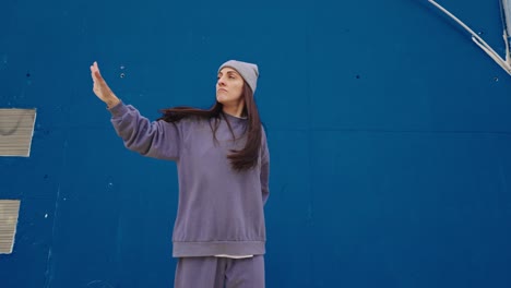 Woman street dancing in front of a blue wall