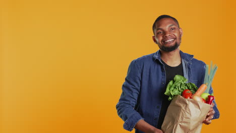 vegano adulto presentando sus productos maduros recién cosechados en una bolsa de papel