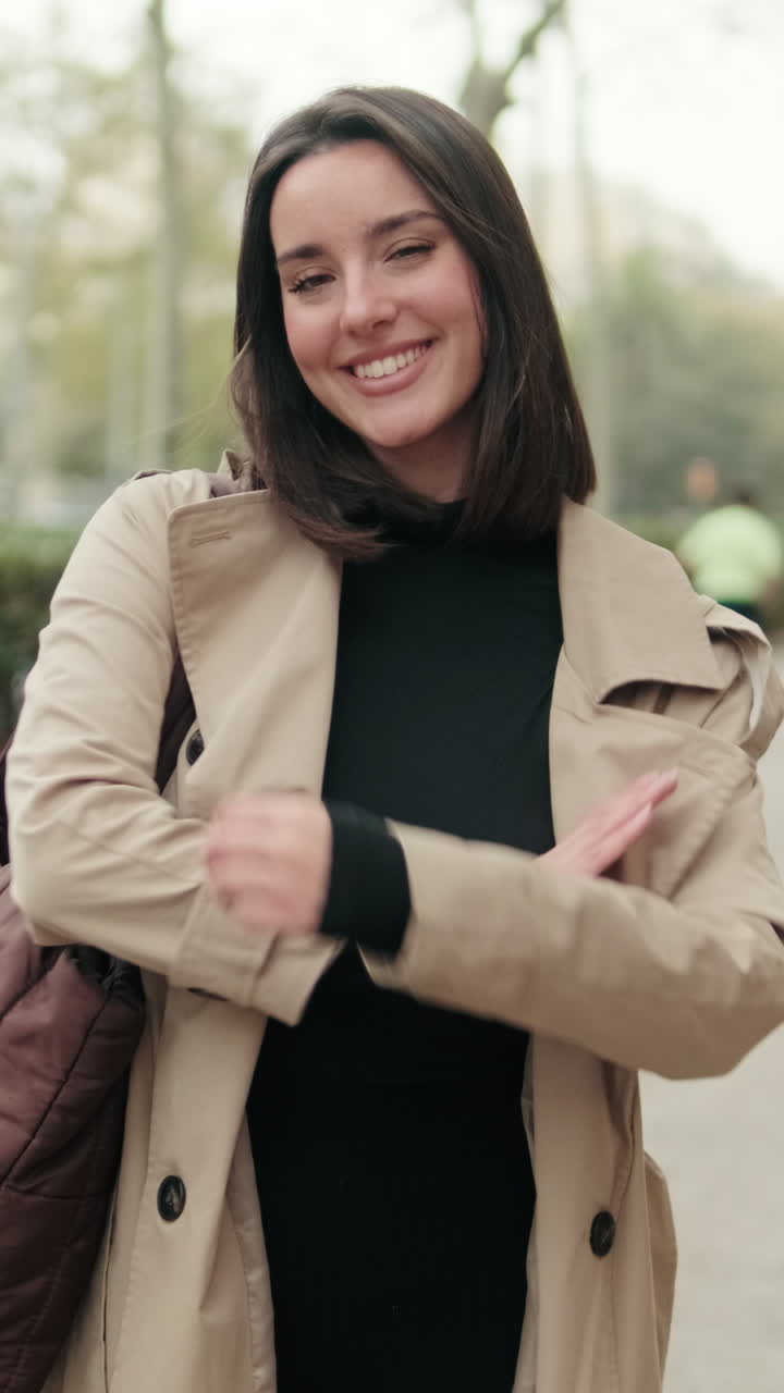 Giovane donna felice in trench che sorride alla macchina fotografica all'aperto
