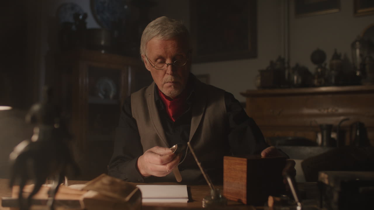 Older passionate man evaluates an old watch in his office at night