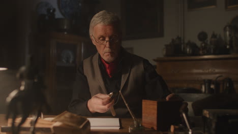 older passionate man evaluates an old watch in his office at night