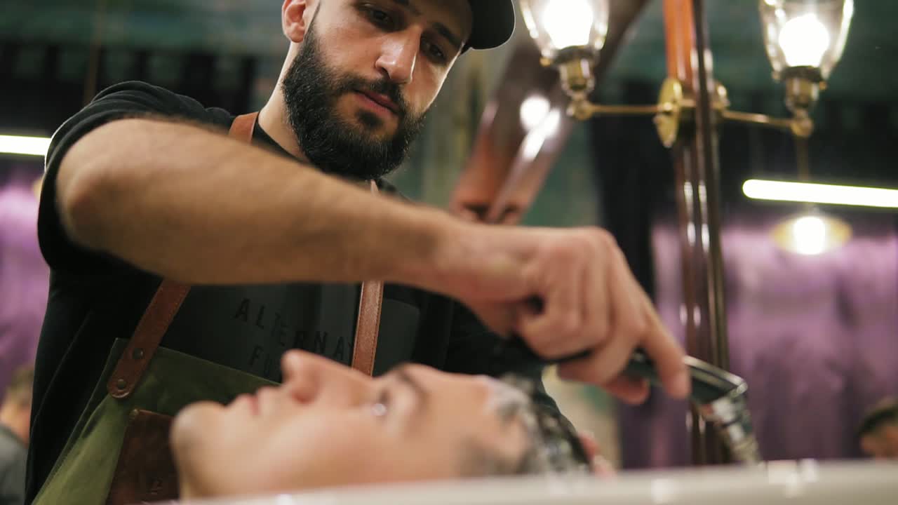 Image of stylish male barber washing hair of his client for making modern haircut in barber shot