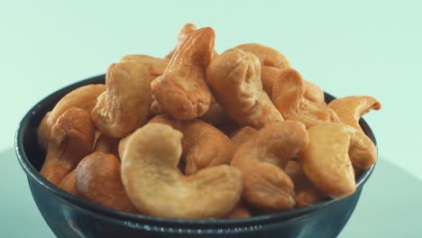 a close up shot of a roasted salty cashews in a black shiny bawl on a rotating stand, slow motion, 4k, man hand taking a cashew of the bawl