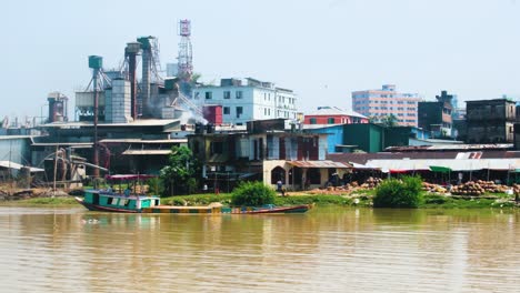 Industrial-factory-at-riverbank-in-Bangladesh-with-a-cargo-ship-carrying-sand-on-the-Surma-river,-Sylhet,-Bangladesh